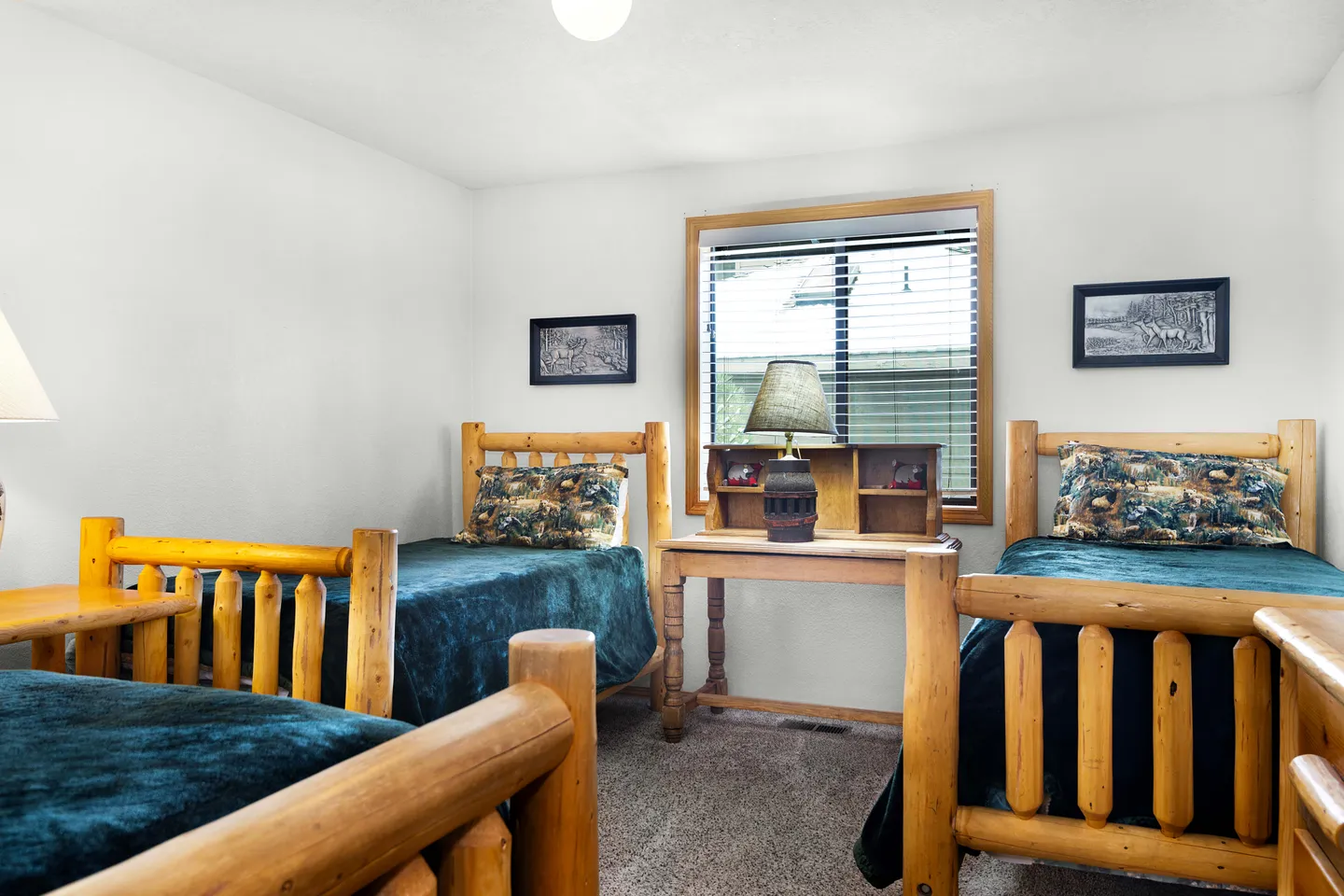 Bedroom with rustic log-frame twin beds, teal bedding, and a small wooden desk by a window.