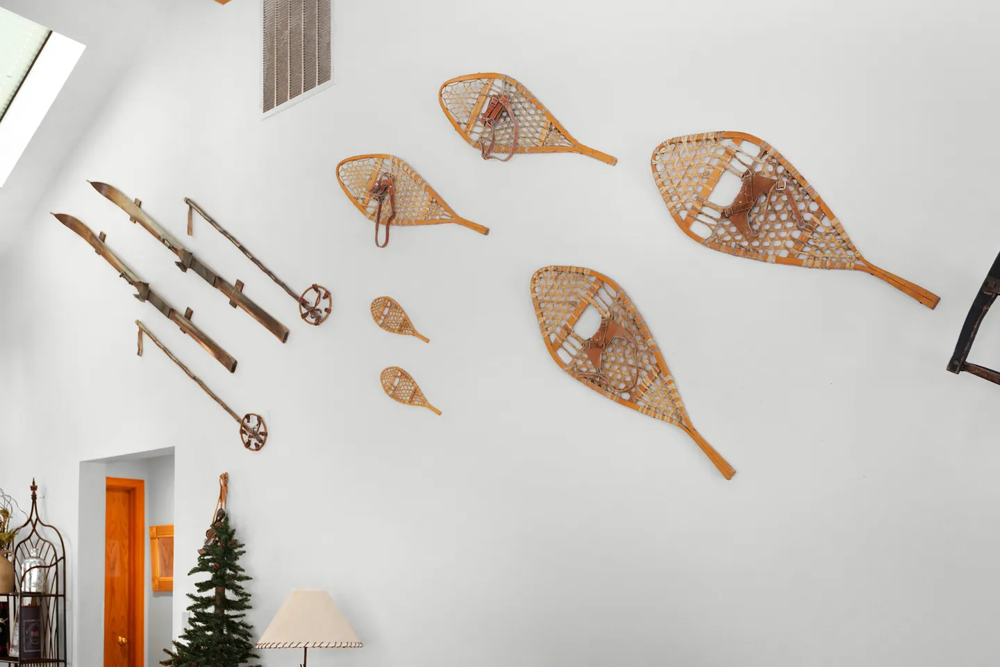 Vintage wooden snowshoes, skis, and ski poles mounted as wall decor on a high white wall beneath a vaulted ceiling.