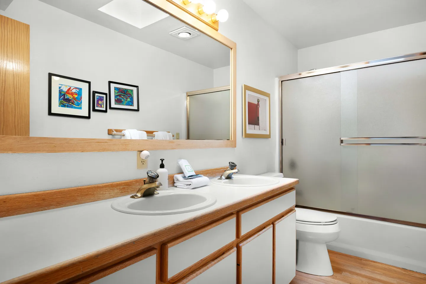 Bathroom featuring a double-sink vanity with a large wood-framed mirror, toilet, and a bathtub with frosted sliding doors.