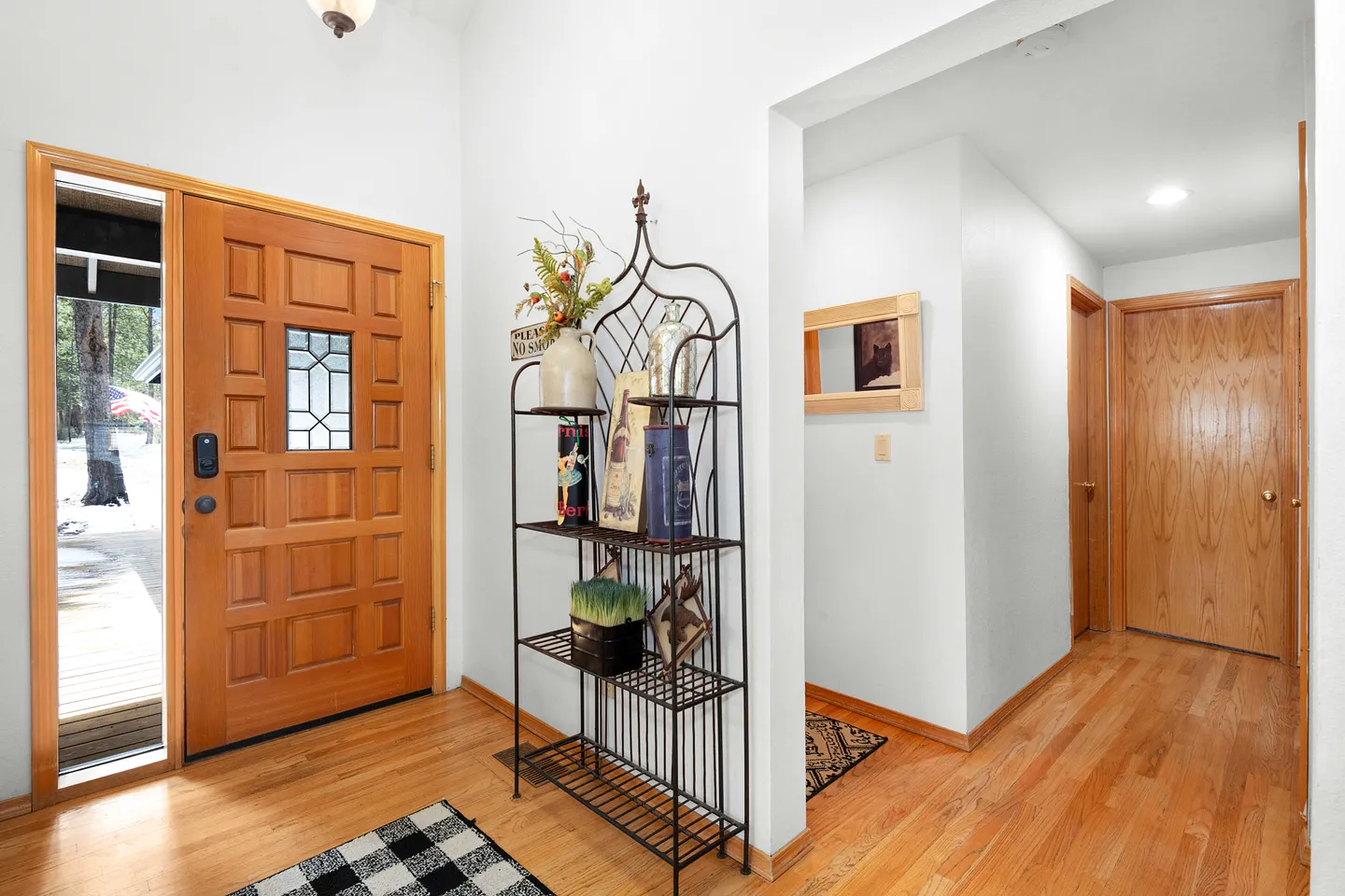 Front entryway with wooden front door, tall metal shelf, wood flooring, and hallway leading to interior doors.