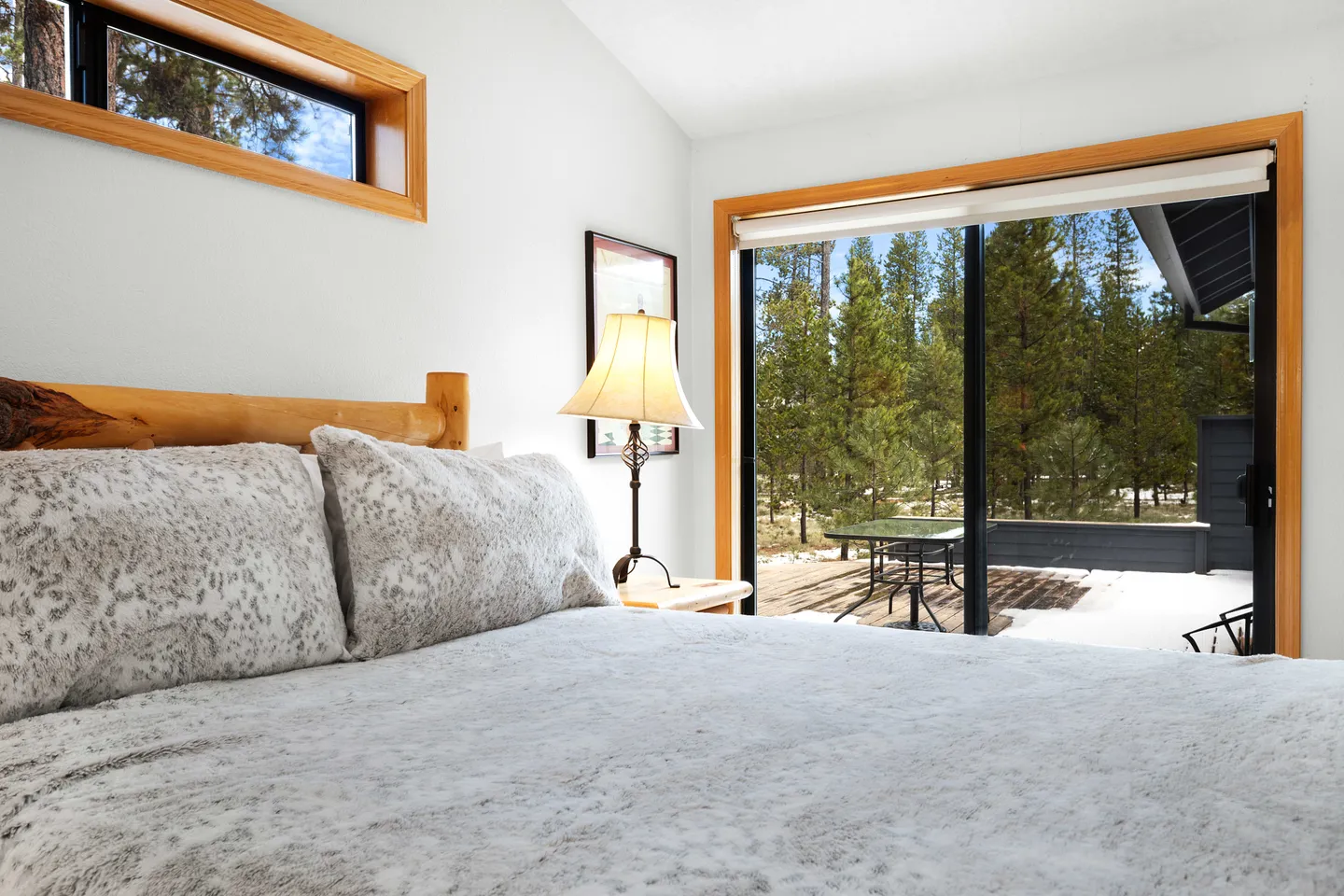 Bedroom with a log-frame bed and sliding glass door leading to a snowy deck and pine trees outside.