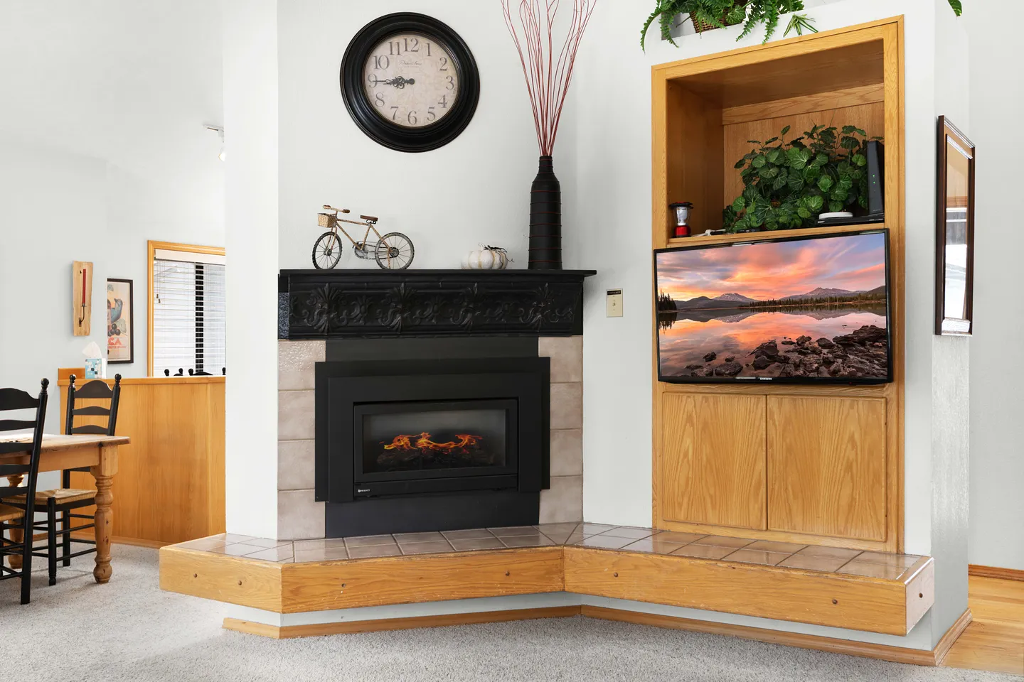 A corner fireplace with a dark mantel next to a built-in wooden entertainment cabinet and television.