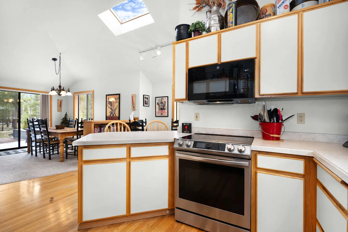 Kitchen with white cabinetry with wood trim, stainless steel oven, and microwave looking toward the dining area.