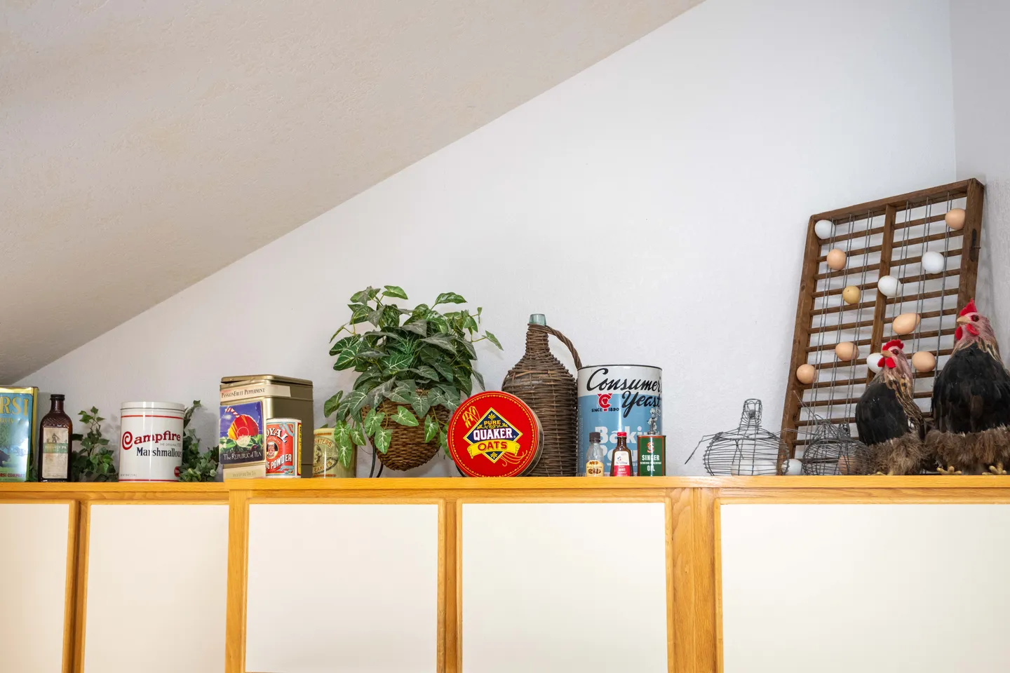 Vintage tins, containers, decorative chickens, and a potted plant displayed atop kitchen cabinets under a vaulted ceiling.