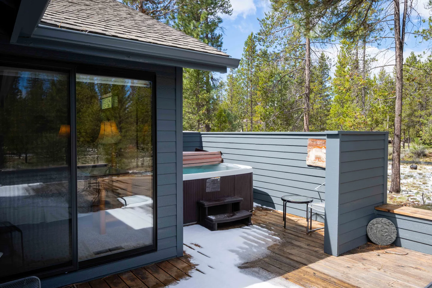 Outdoor wooden deck featuring a hot tub enclosed by a blue privacy fence, adjacent to glass patio doors.