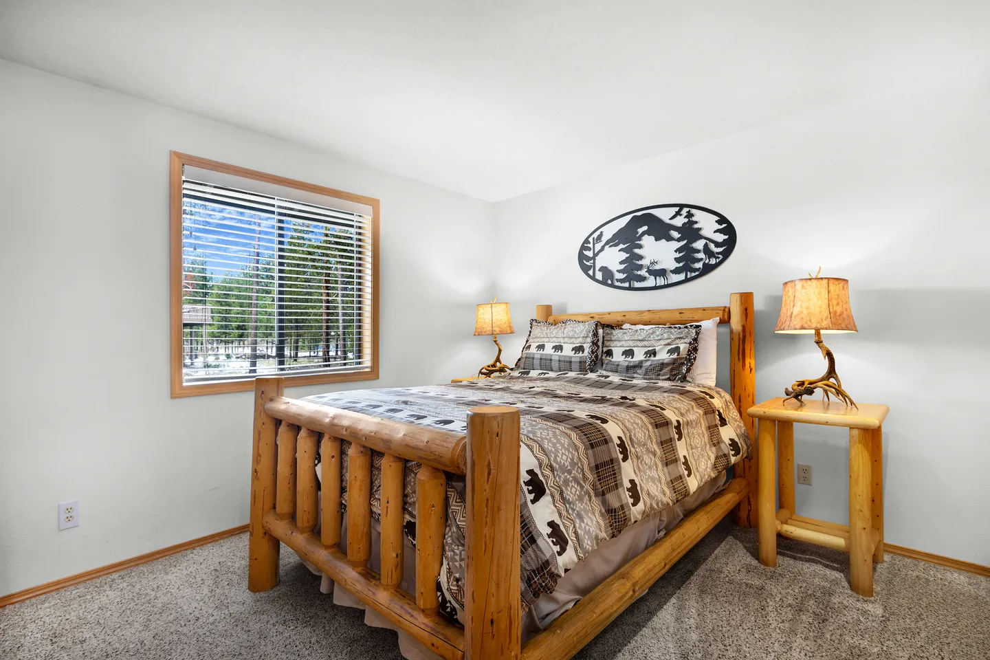 Bedroom with a rustic log-frame bed, matching nightstands with antler-style lamps, and a window with blinds looking outdoors.