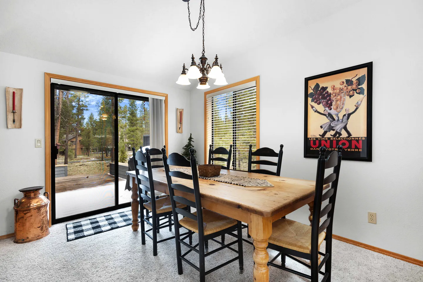 Dining area with a wooden table, black chairs, chandelier, sliding glass door leading to a deck, and window with blinds.