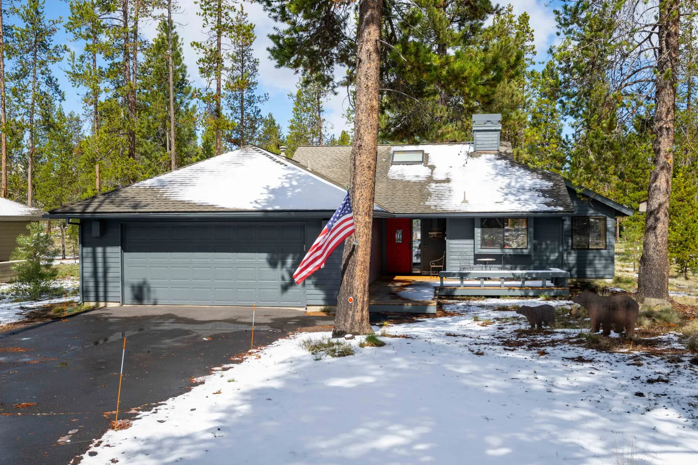 Exterior view of a single-story gray home with a two-car garage, front porch, and snow on the roof and ground.