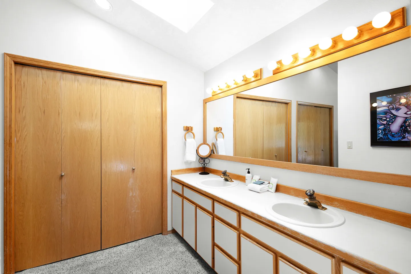 Bathroom vanity with two sinks, a wide mirror with vanity strip lighting, and wooden double doors.