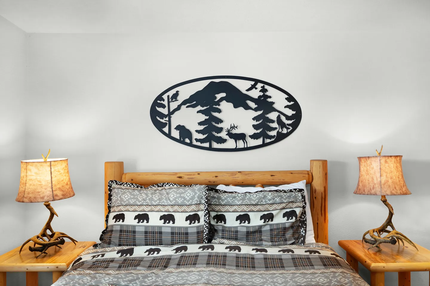 Bedroom featuring a wooden log headboard, bear-themed bedding, antler-style bedside lamps, and a silhouette metal wall sculpture above the bed.