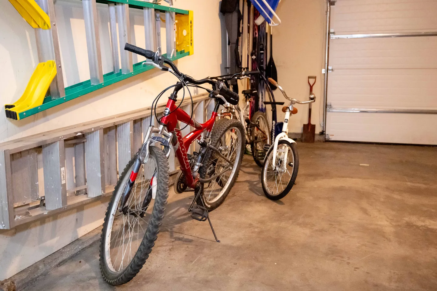 A garage with bicycles parked on a concrete floor next to wall-mounted ladders.