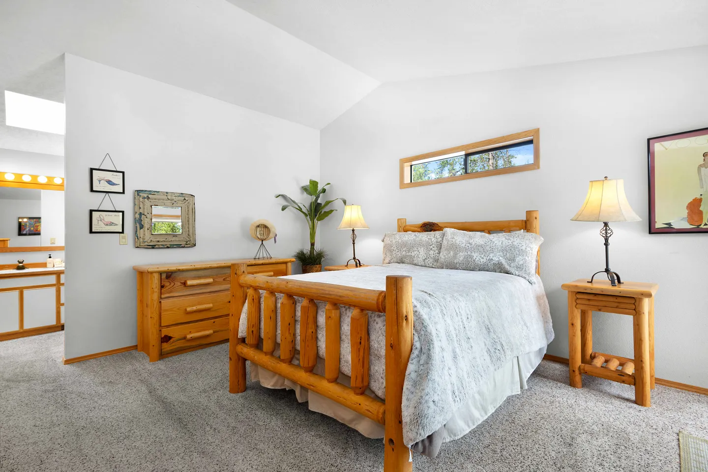 Bedroom featuring a log-style wooden bed, matching nightstand and dresser, carpeted flooring, and an adjoining open vanity area.