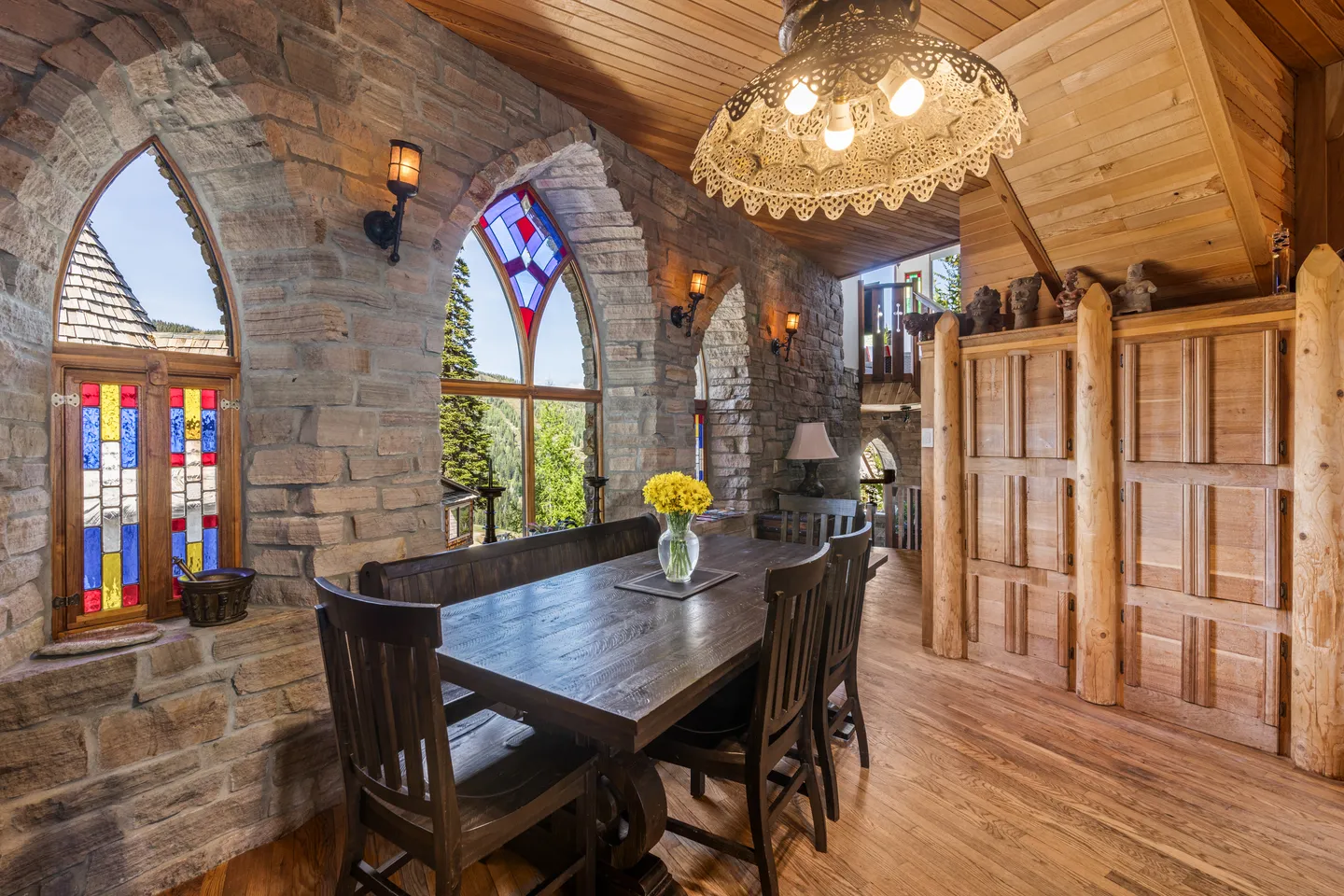Dining area with a wooden table, bench, stone walls, and arched stained-glass windows.