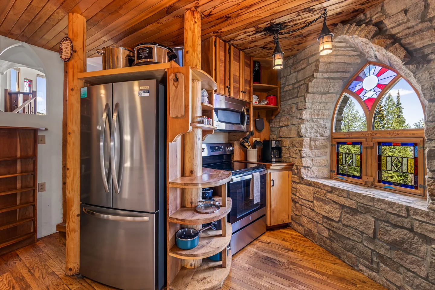 Kitchen corner featuring stainless steel appliances, log and wood cabinetry, and an arched stone wall with stained-glass windows.