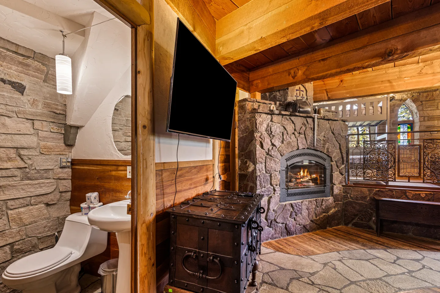 Rustic living area featuring a stone fireplace and wall-mounted TV adjacent to an open bathroom doorway.
