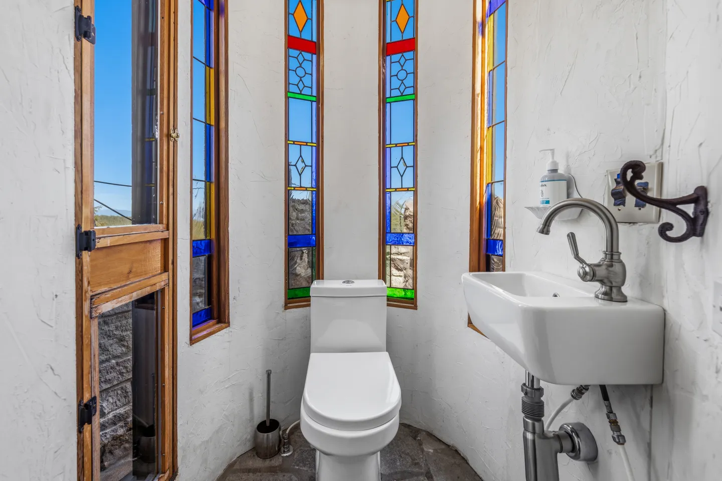 A compact bathroom nook with a white toilet, small wall-mounted sink, and tall narrow stained glass windows.