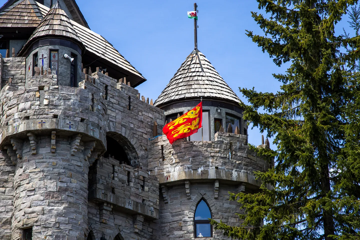 Exterior stone turret and crenellated battlements of a castle-style building flying flags against a blue sky.