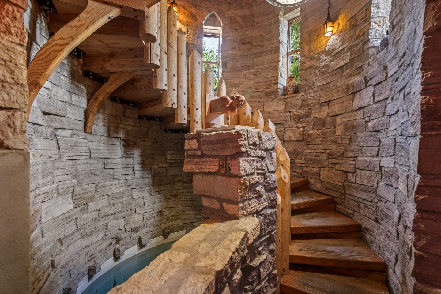 Spiral staircase with wooden steps and stone-clad walls inside a tower-style room overlooking an indoor water feature.