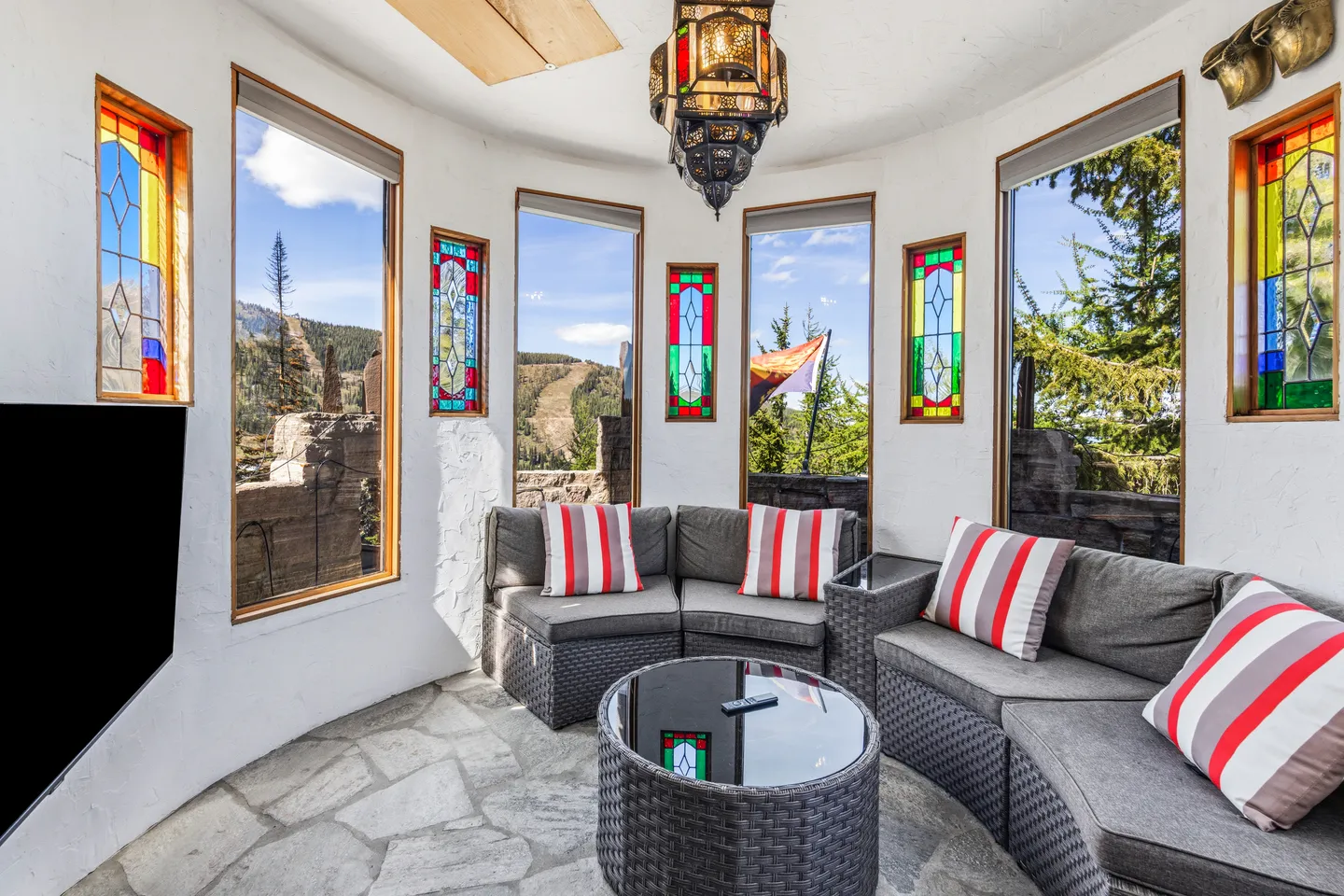 Curved sunroom sitting area with stone flooring, curved wicker sectional sofa, round coffee table, and windows interspersed with stained glass panels.