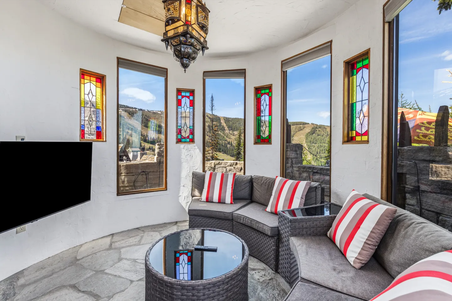Sunroom lounge featuring curved sectional seating, flagstone flooring, stained glass accents, and scenic mountain views through multiple windows.