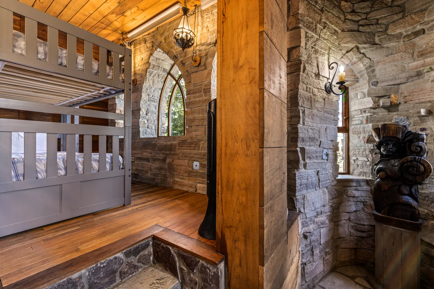 Bedroom area with rustic stone walls, hardwood floors, a bunk bed, and an arched window.