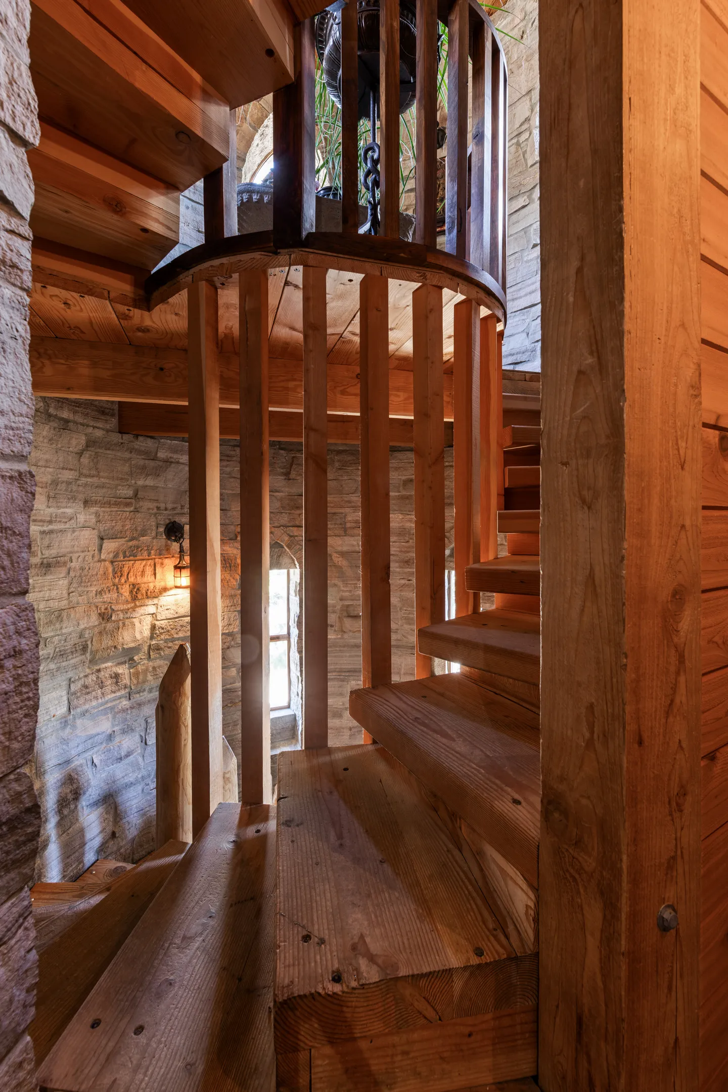 A wooden spiral staircase enclosed within a stone-walled tower with narrow arched windows.