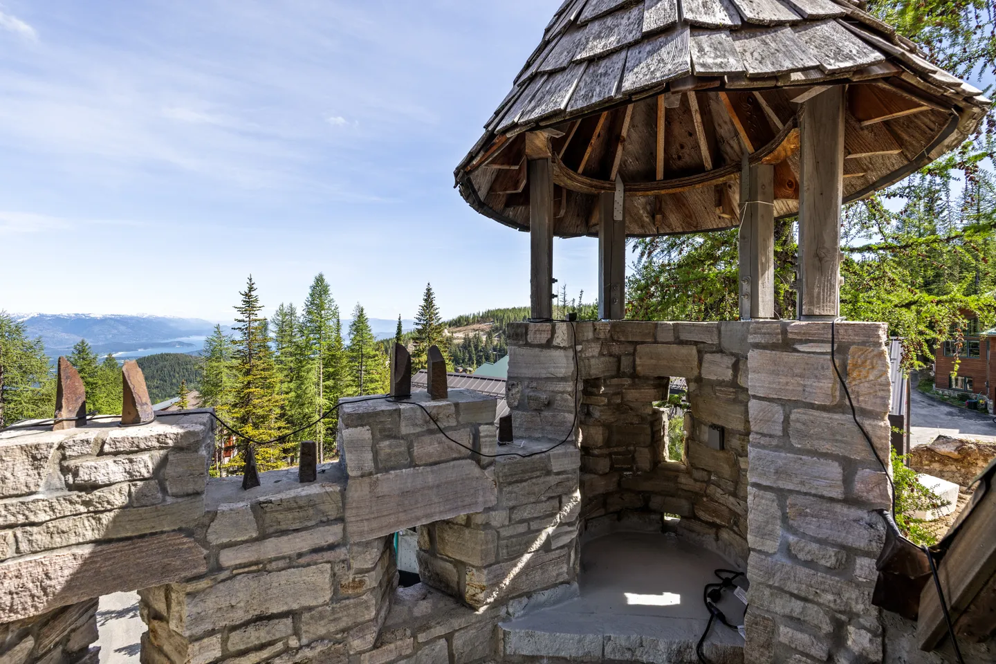 Stone turret with a conical shingled roof overlooking evergreen trees and distant mountains.