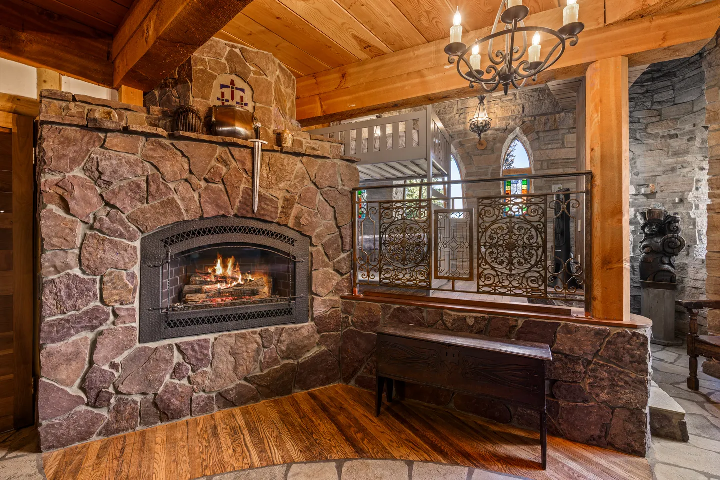 A stone fireplace with a lit fire next to decorative iron railings and timber beams.