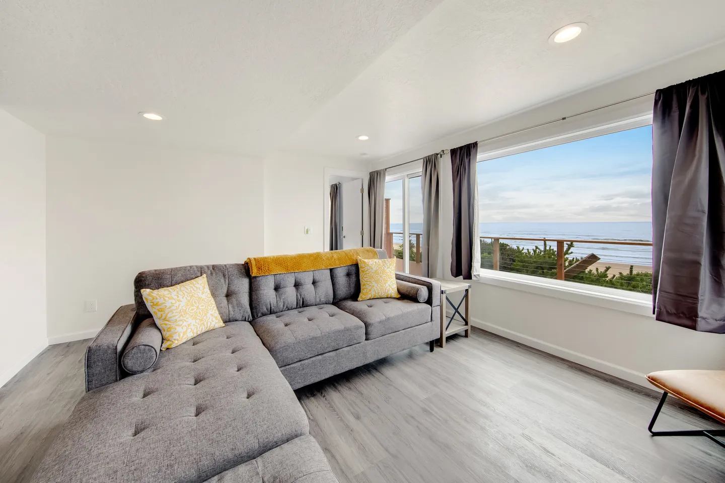 Living room featuring a grey sectional sofa and large picture windows looking out to the ocean and coastline.