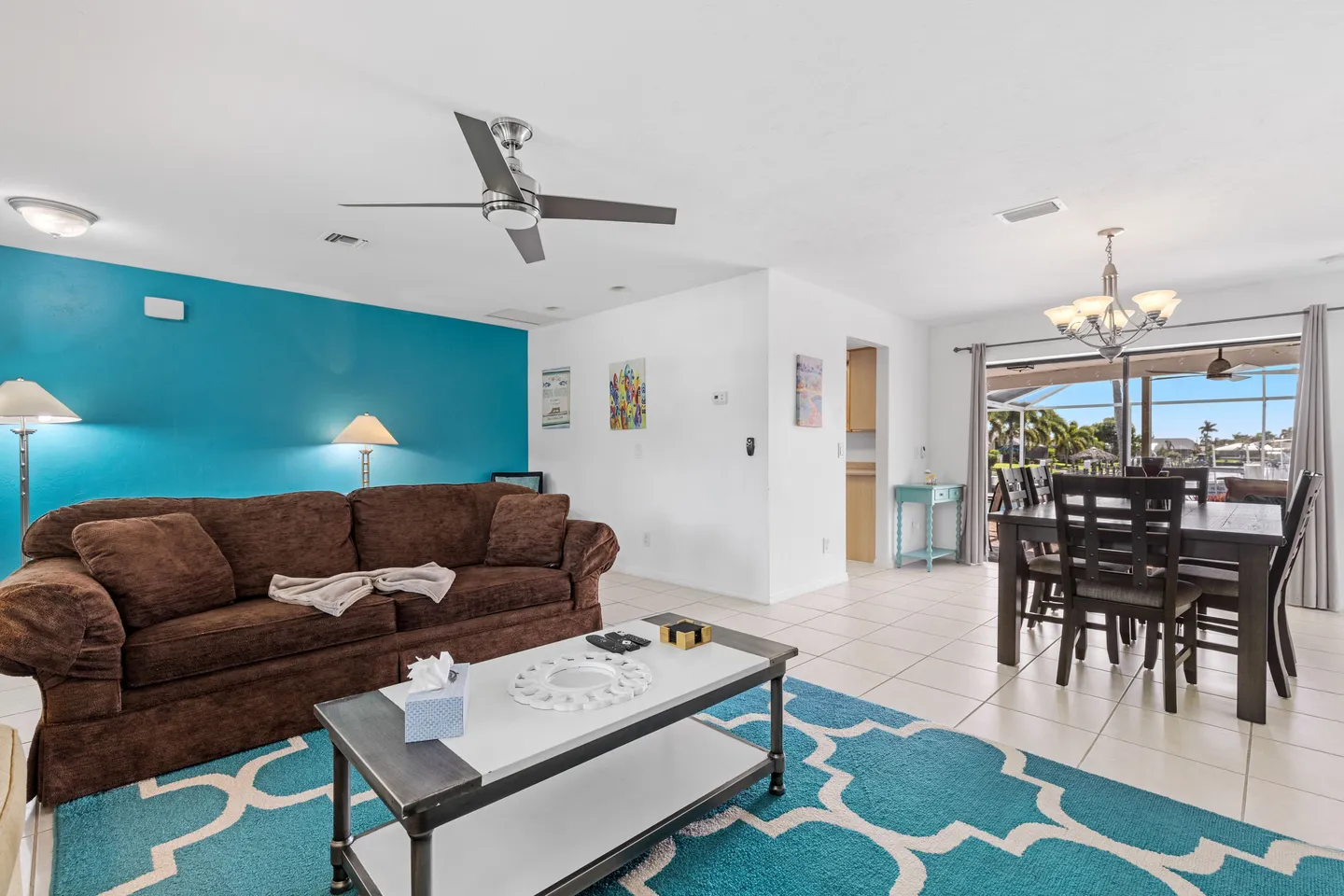 Open living and dining area with a brown couch, teal accent wall, and dining table set by sliding glass doors.