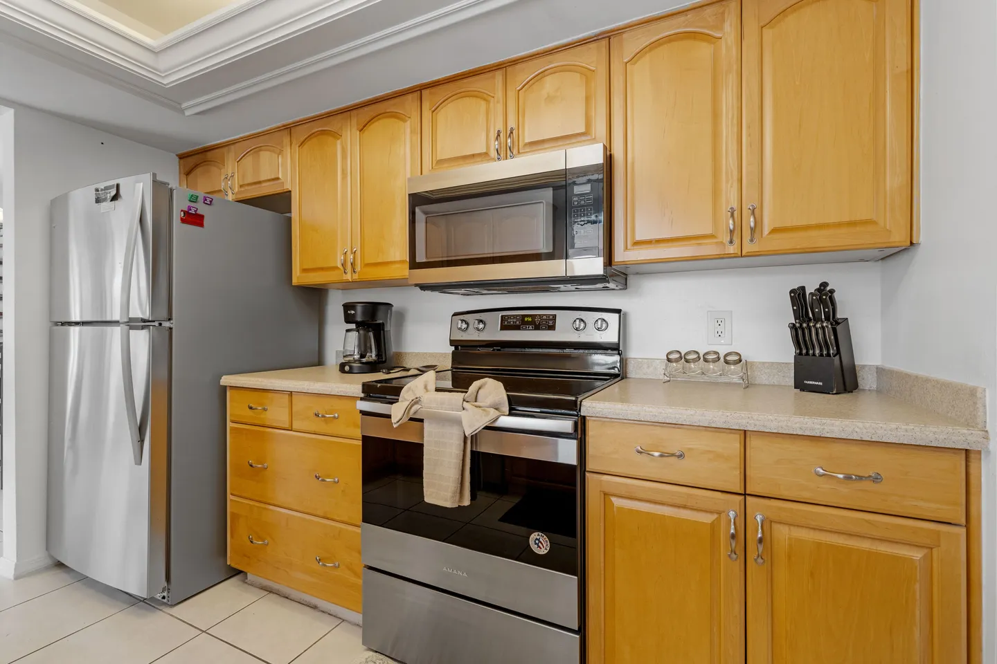 Kitchen counter area with light wood cabinets, stainless steel appliances, and a tiled floor.