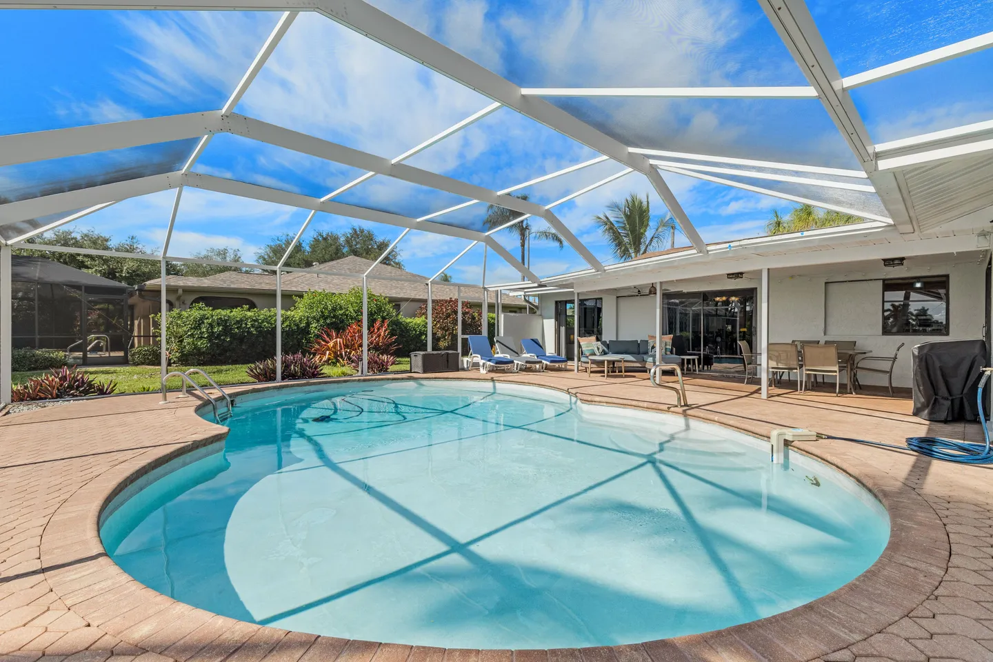 Screened pool enclosure with a curved swimming pool, paved patio, and outdoor patio furniture.