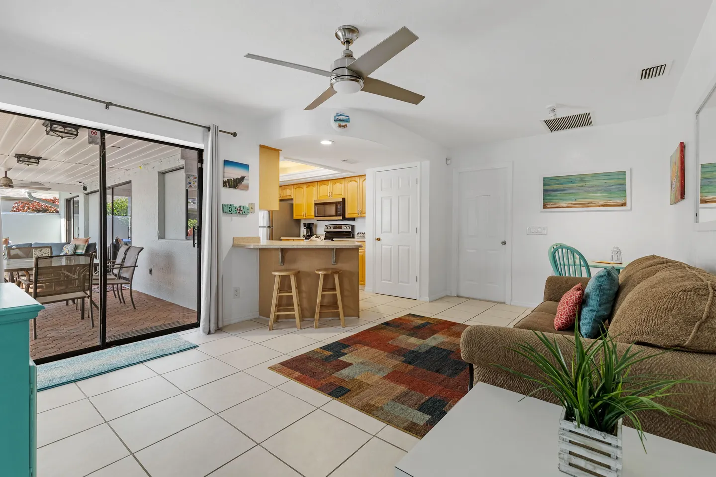 Open-concept living room with tile floors, a ceiling fan, a sofa, and a breakfast bar opening to the kitchen, alongside sliding doors leading to a patio.
