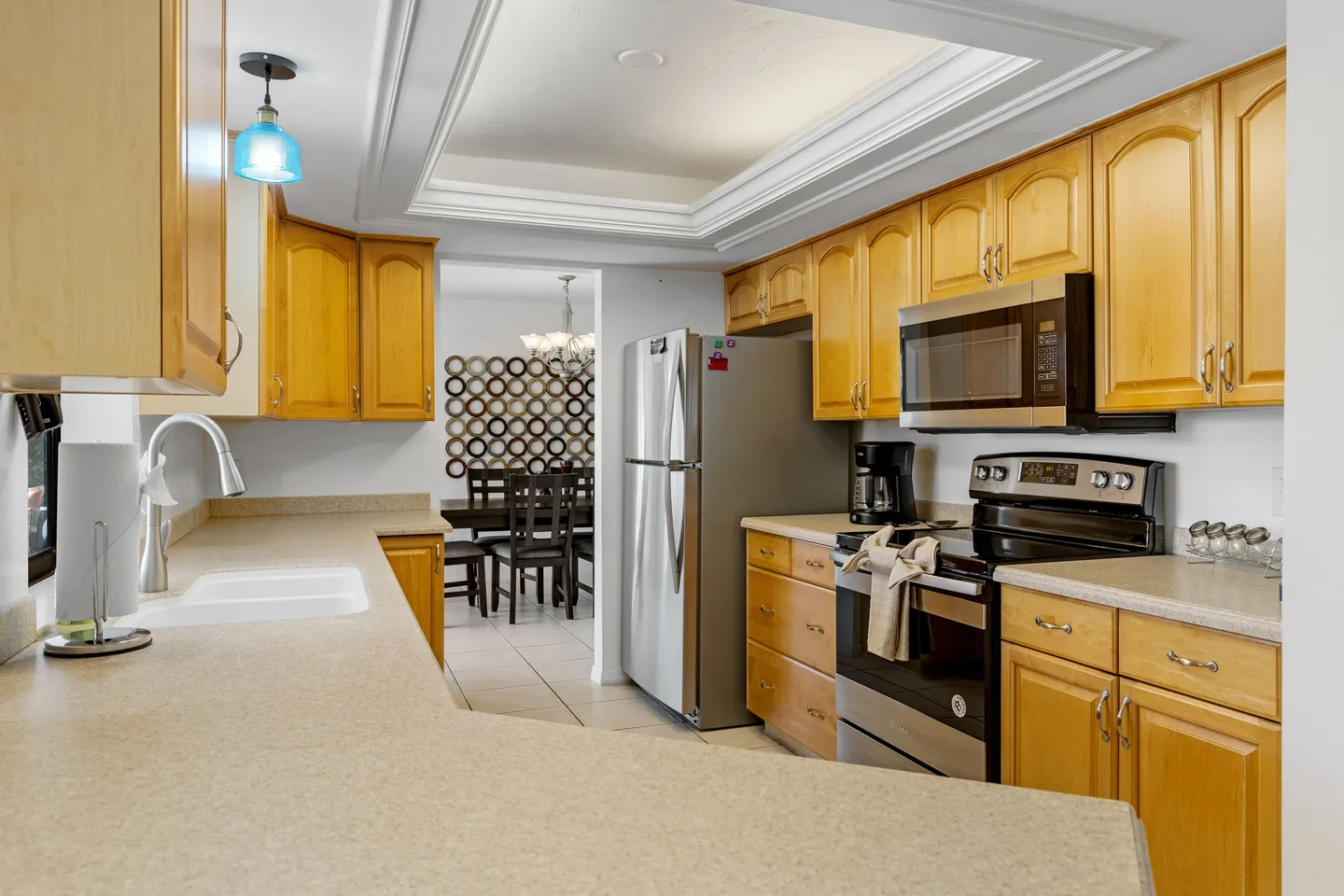 Kitchen with light wood cabinets, light countertops, and stainless steel appliances looking through to the dining area.