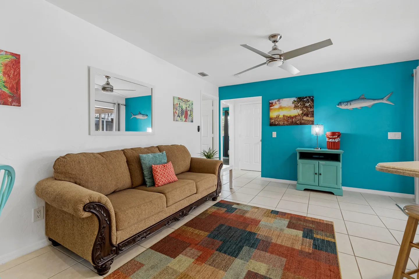 Living area with a brown upholstered sofa, colorful area rug, tile flooring, and a bright turquoise accent wall.