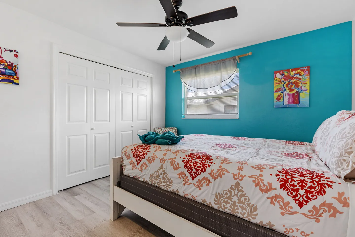 Bedroom featuring a turquoise accent wall, a bed with an ornate patterned cover, and white closet doors.