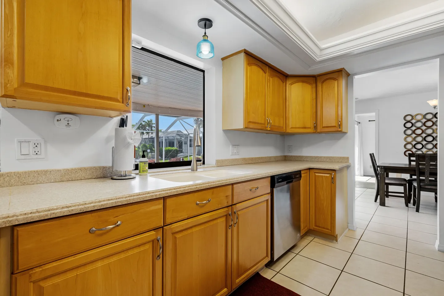 Kitchen with wooden cabinets, light-colored countertops, a window overlooking a screened patio, and a stainless steel dishwasher.
