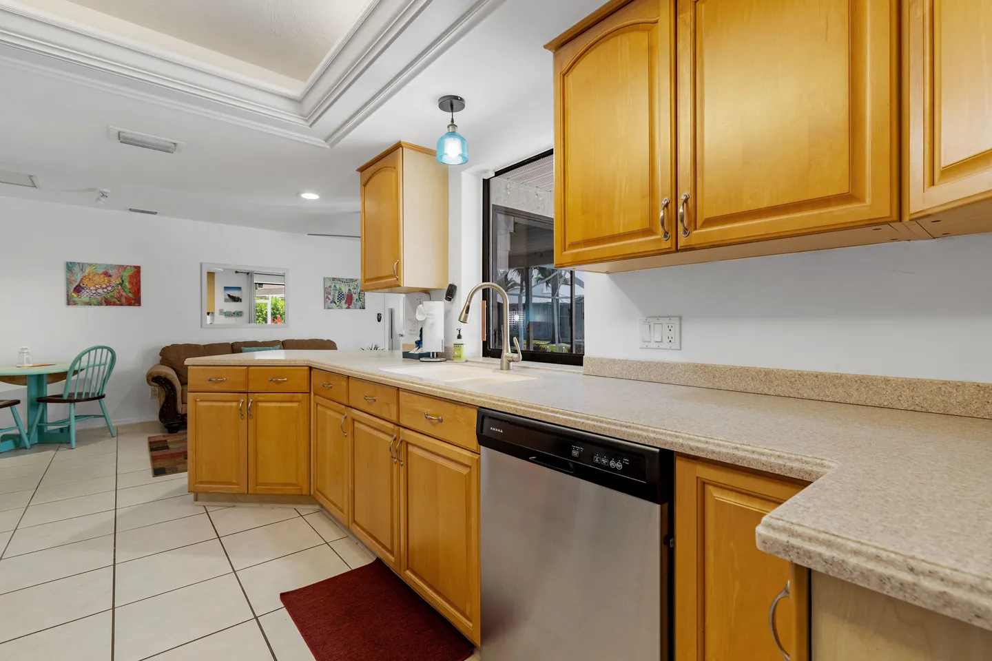 Kitchen counter with light wood cabinets, speckled countertop, stainless steel dishwasher, and window over the sink.