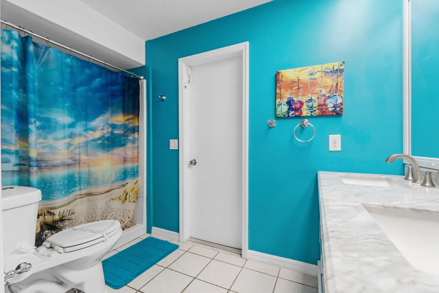 Bathroom featuring turquoise blue walls, tiled floor, a vanity with a marbled countertop, and a shower curtain showing a beach scene.