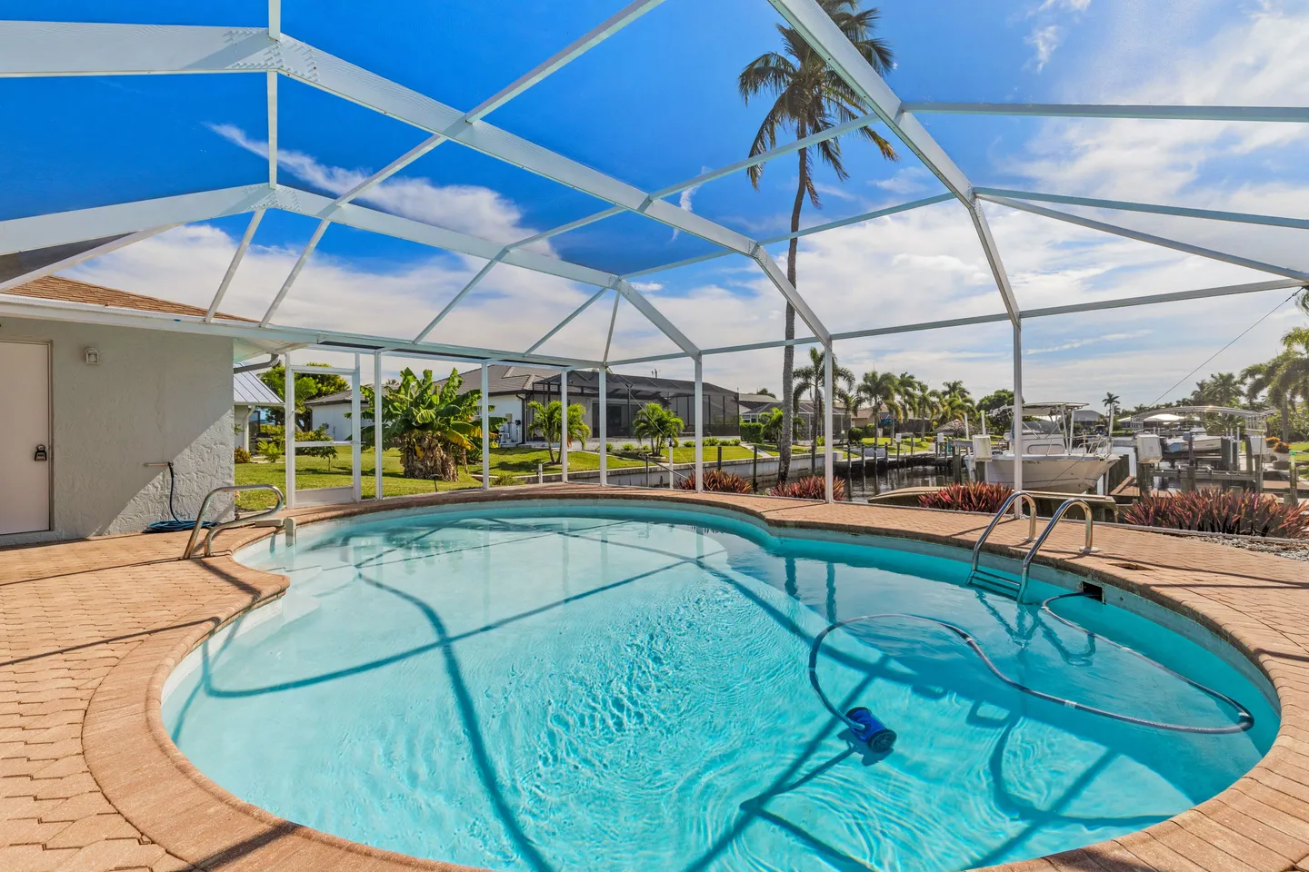 Screened-in outdoor swimming pool overlooking a canal lined with palm trees and houses.
