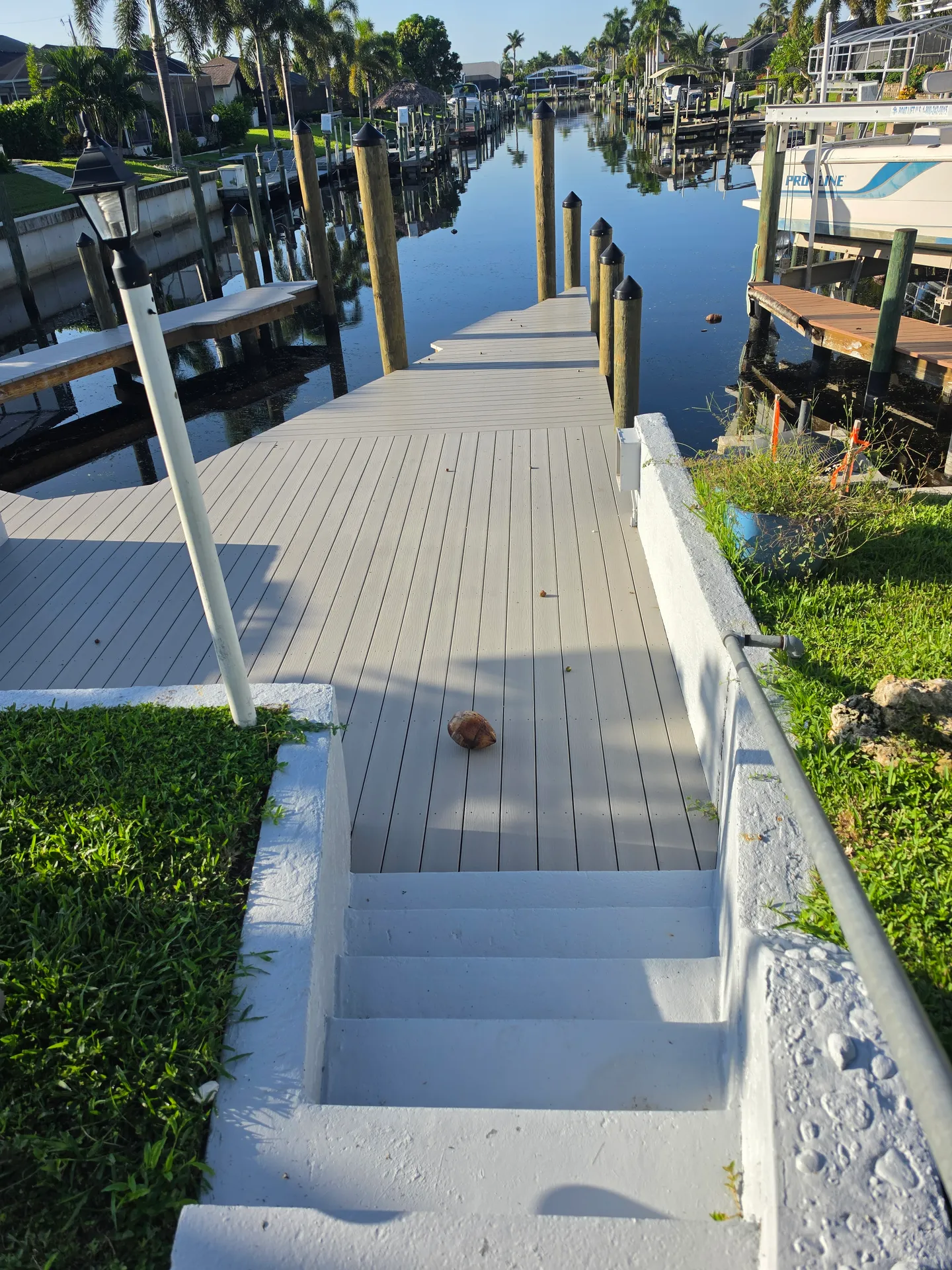 Concrete steps leading down to a boat dock along a residential canal with pilings and nearby boats.