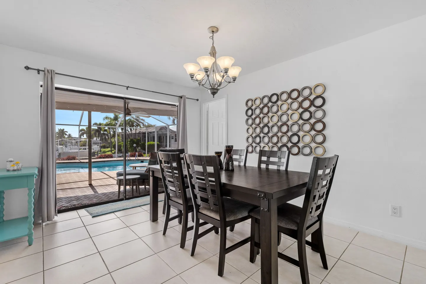 Dining area with a dark wood table and chairs next to sliding glass doors opening to a screened pool patio.