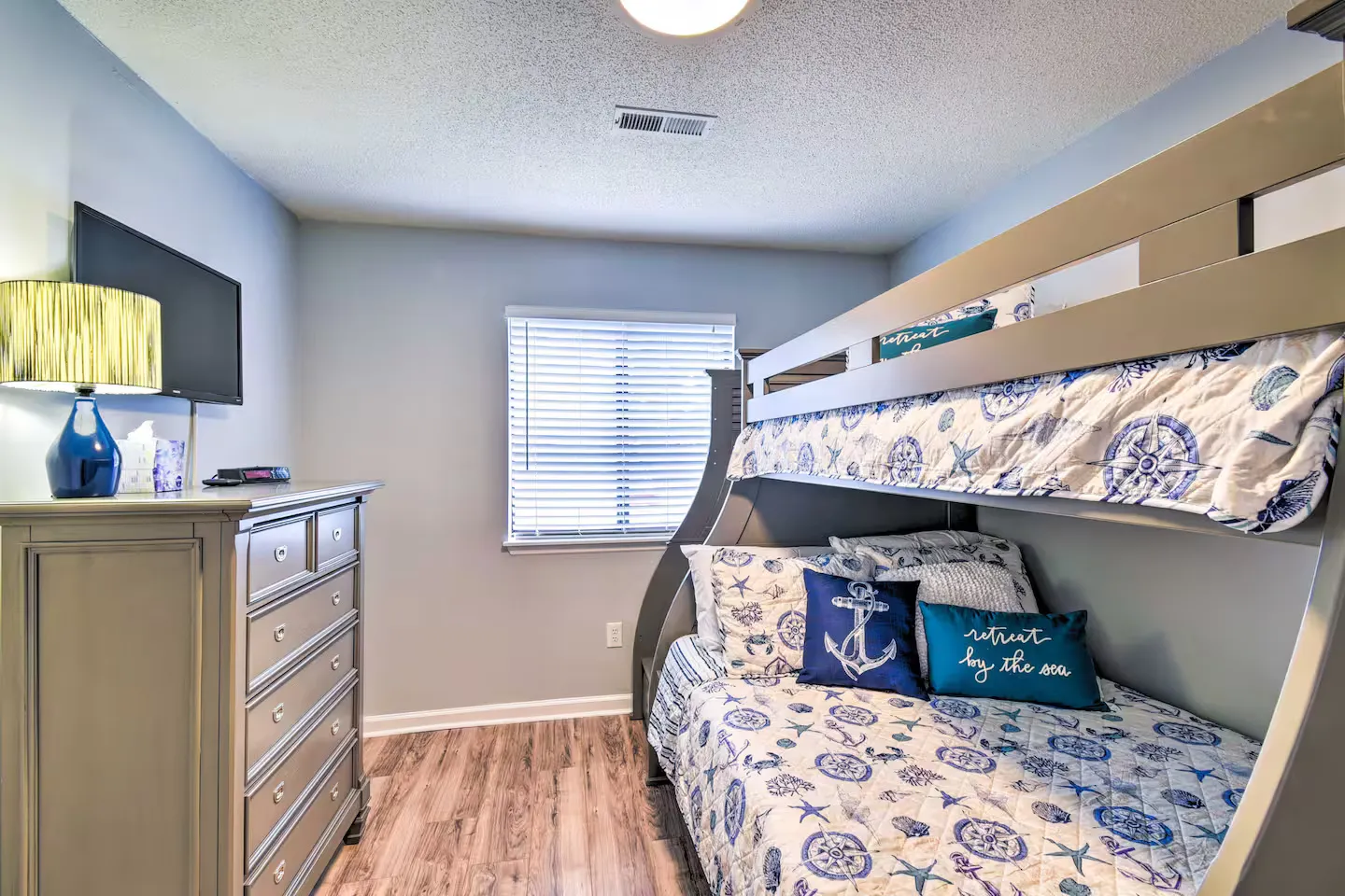 Bedroom featuring a wooden bunk bed with coastal bedding, a tall dresser, a mounted TV, and wood-look flooring.