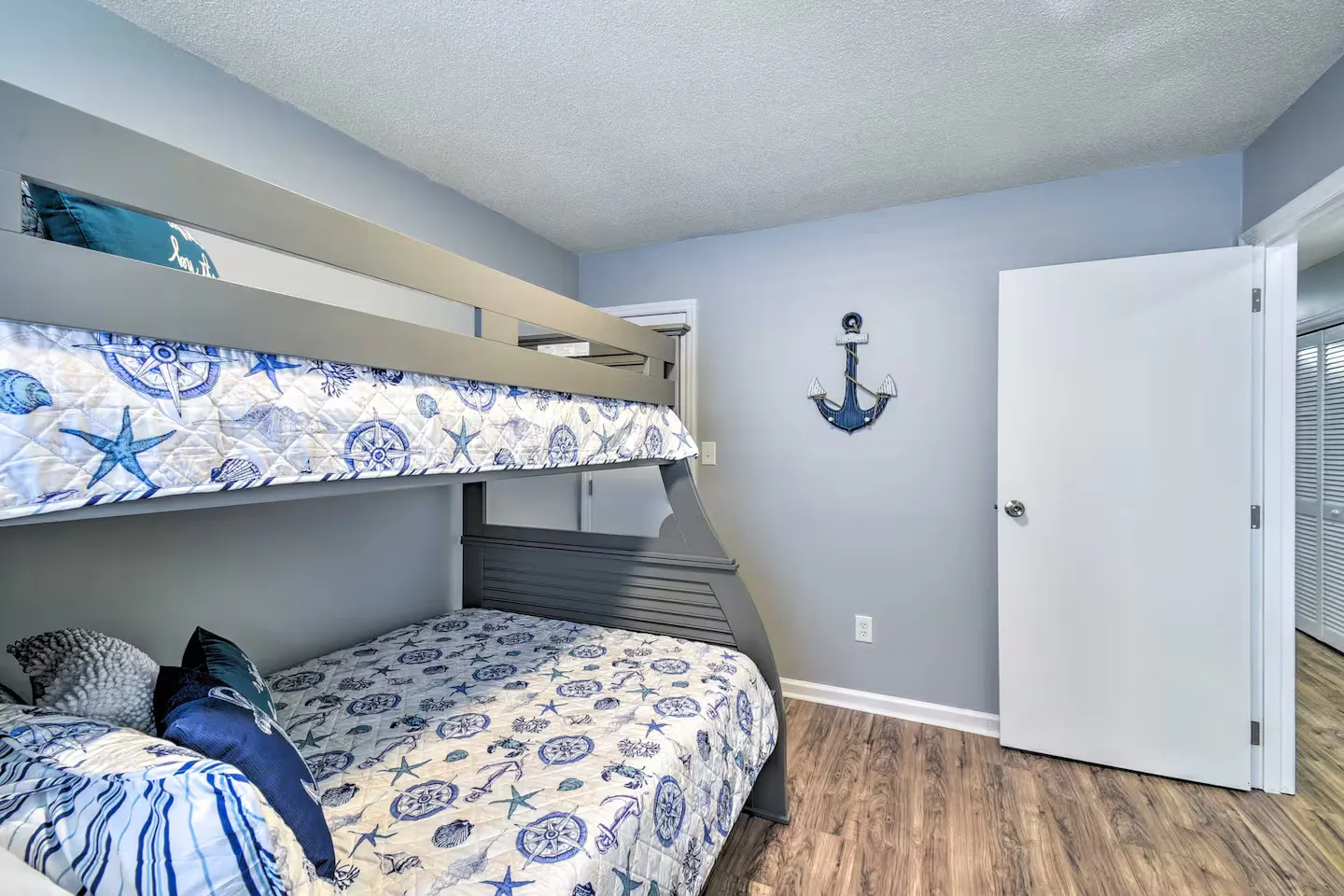 Bedroom with gray painted walls, wood-look flooring, and a gray bunk bed dressed in nautical-themed bedding.