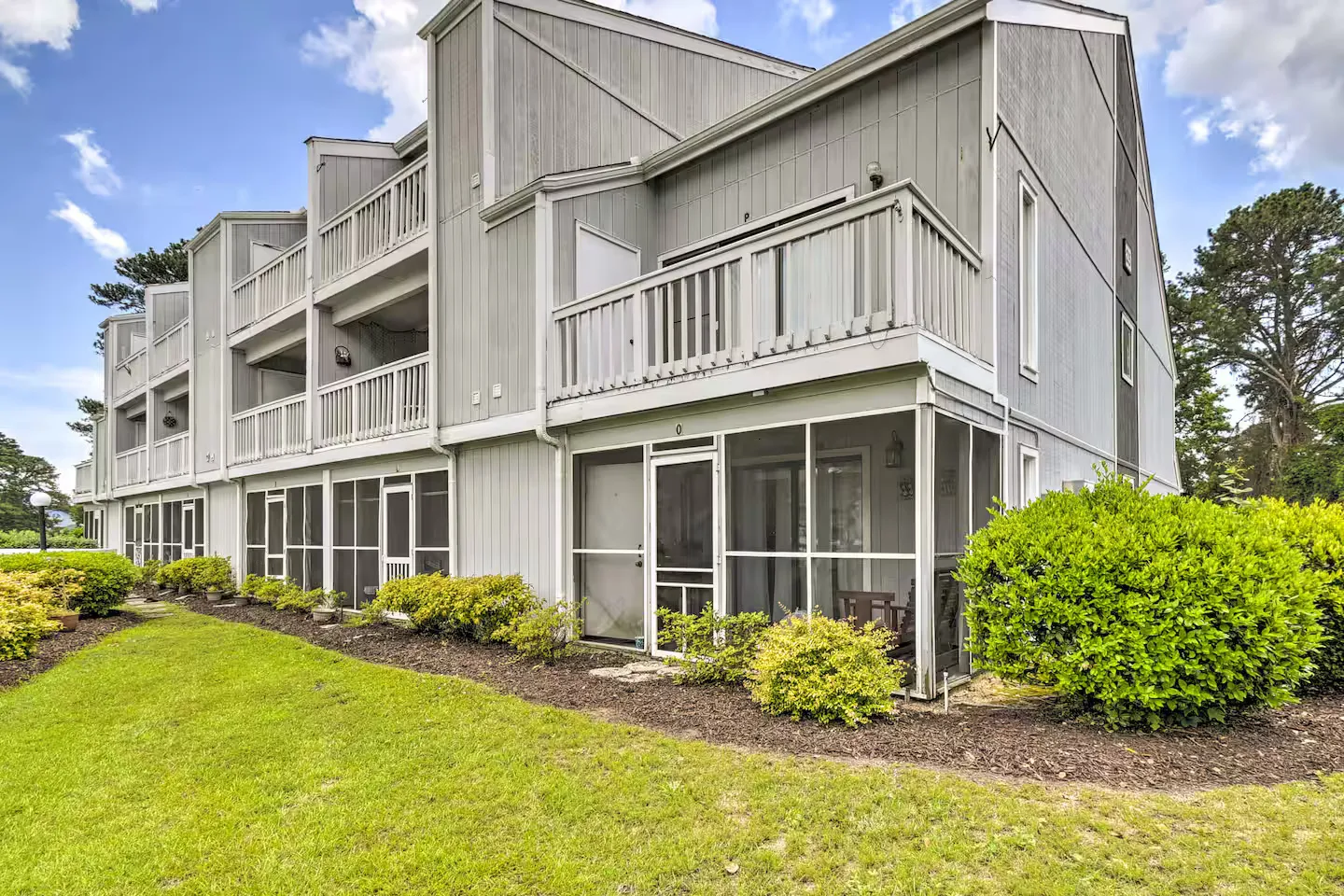 Exterior view of multi-unit residential building with screened-in porches and upper-level balconies alongside a green lawn.