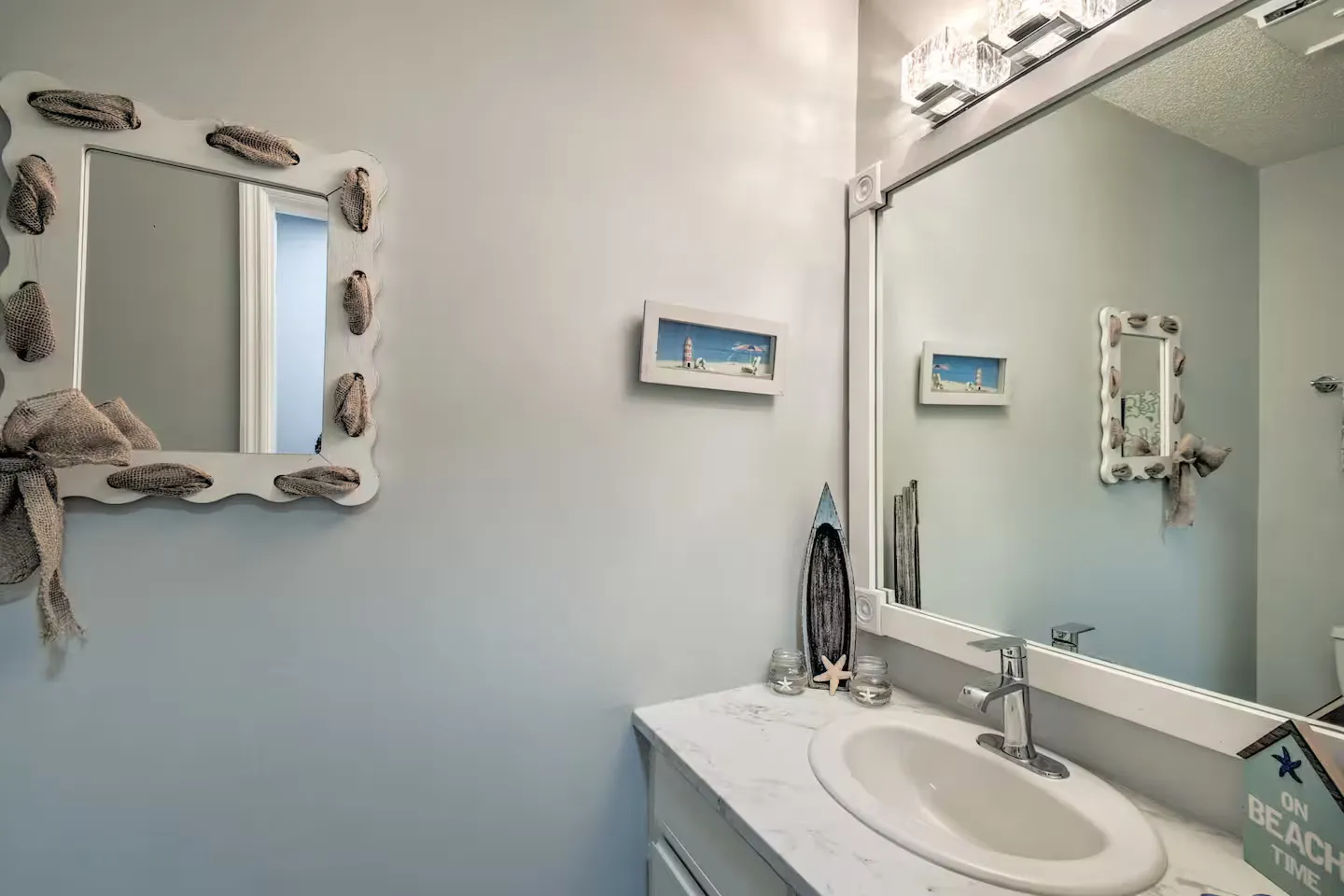 Bathroom vanity with a white oval sink, marbled countertop, large vanity mirror, and decorative wall mirror.