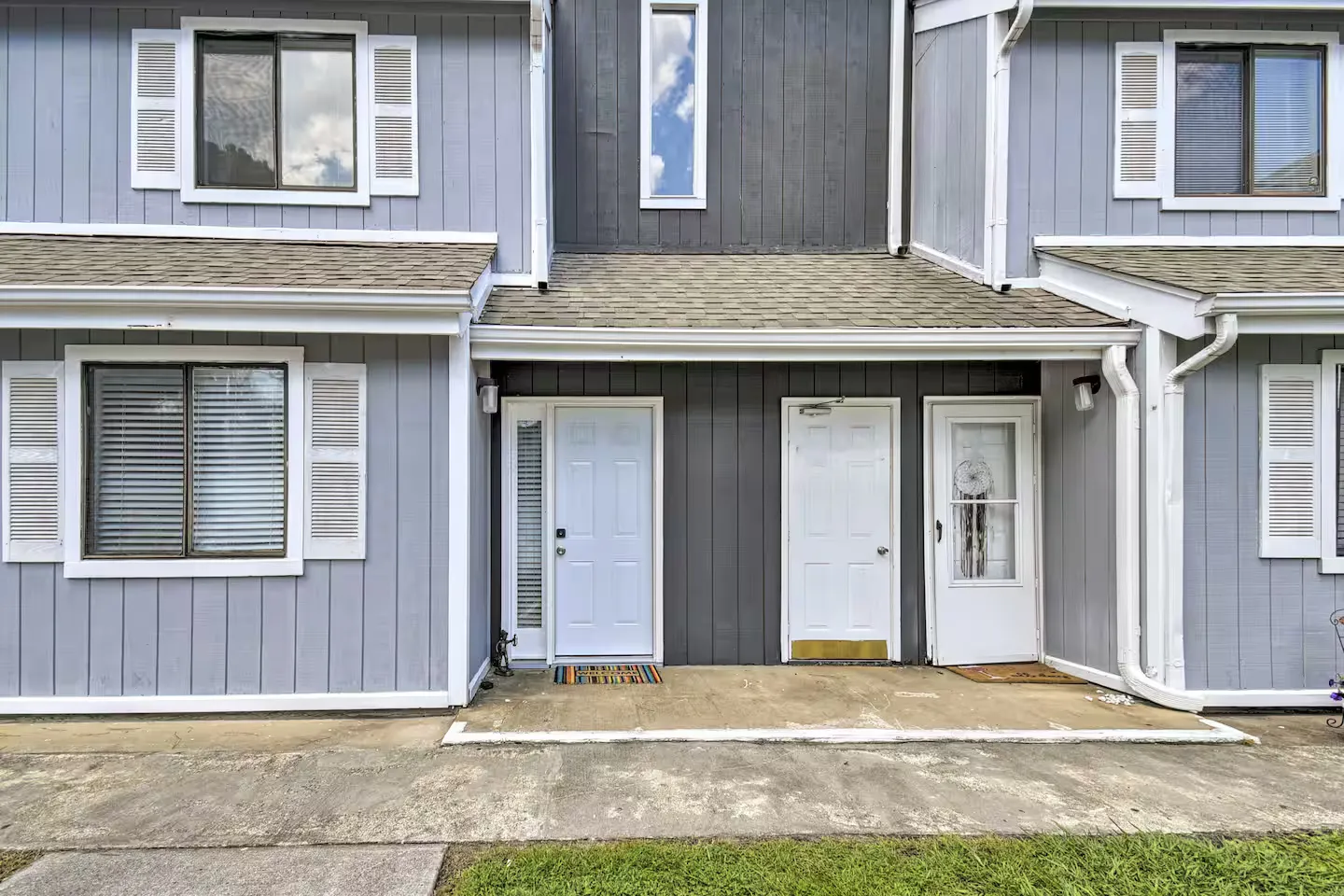 Exterior front entrance of a multi-unit townhouse featuring gray siding, white doors, and white window shutters.
