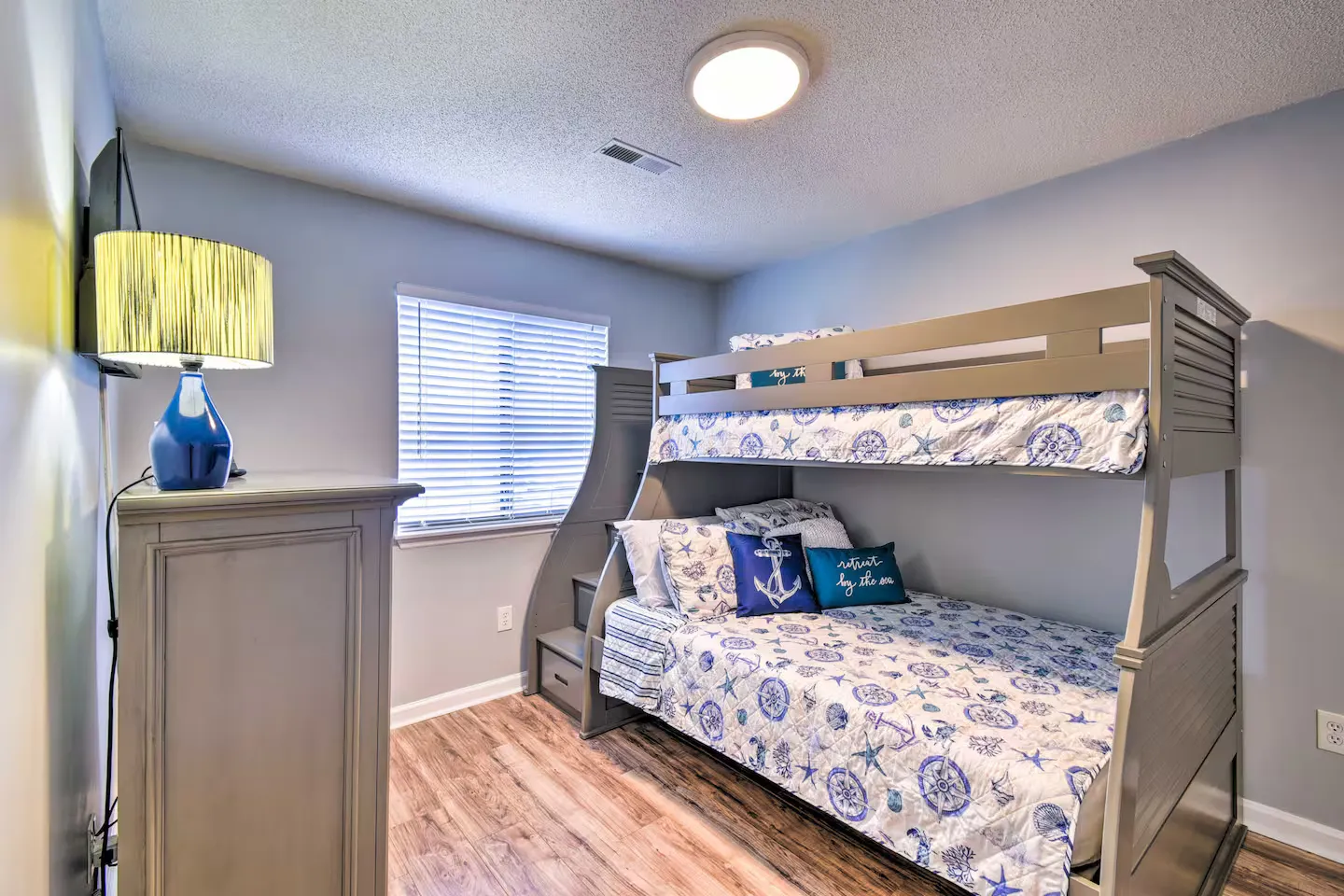 Bedroom featuring a gray bunk bed with nautical-themed bedding, a dresser, and a window with blinds.
