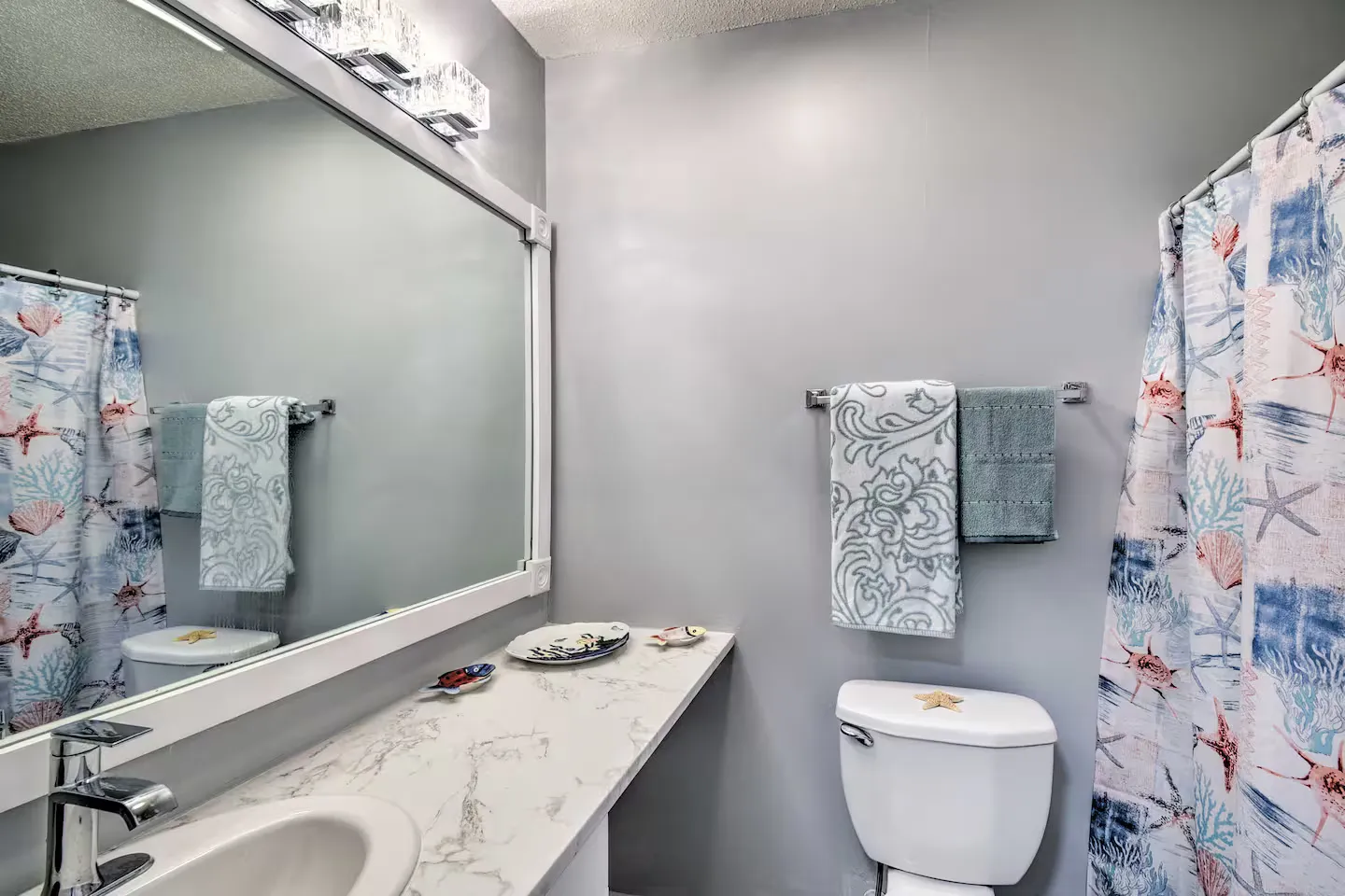 Bathroom featuring a vanity with a large framed mirror, toilet, and an ocean-themed shower curtain.