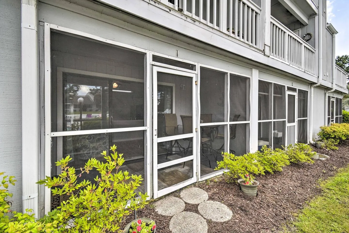 Exterior view of a ground-floor screened porch with a screen door and outdoor seating visible inside.